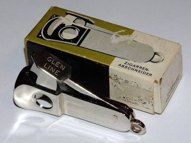 A vintage guillotine-style cigar cutter beside its original box