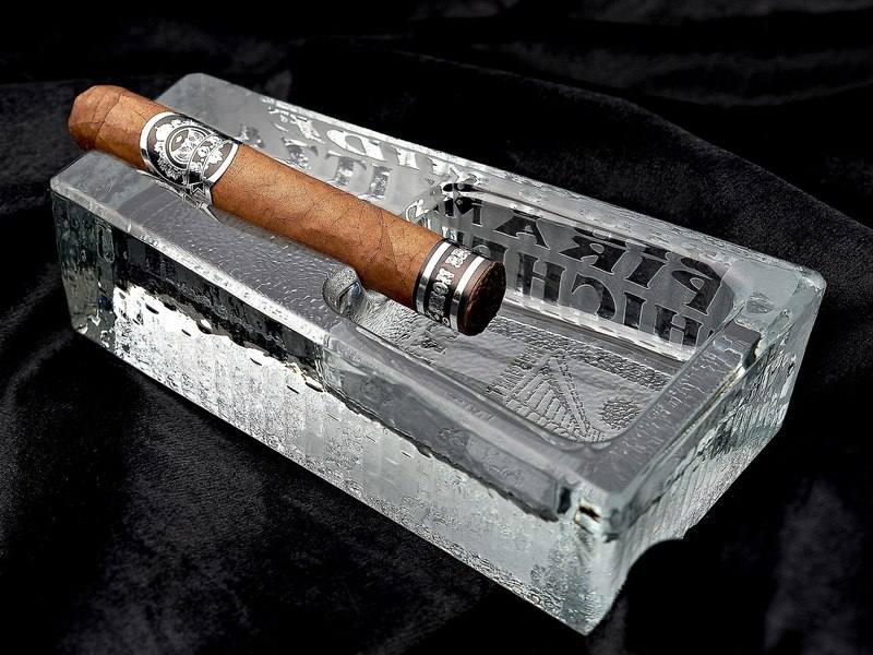 A lit cigar resting in a glass ashtray against a dark background