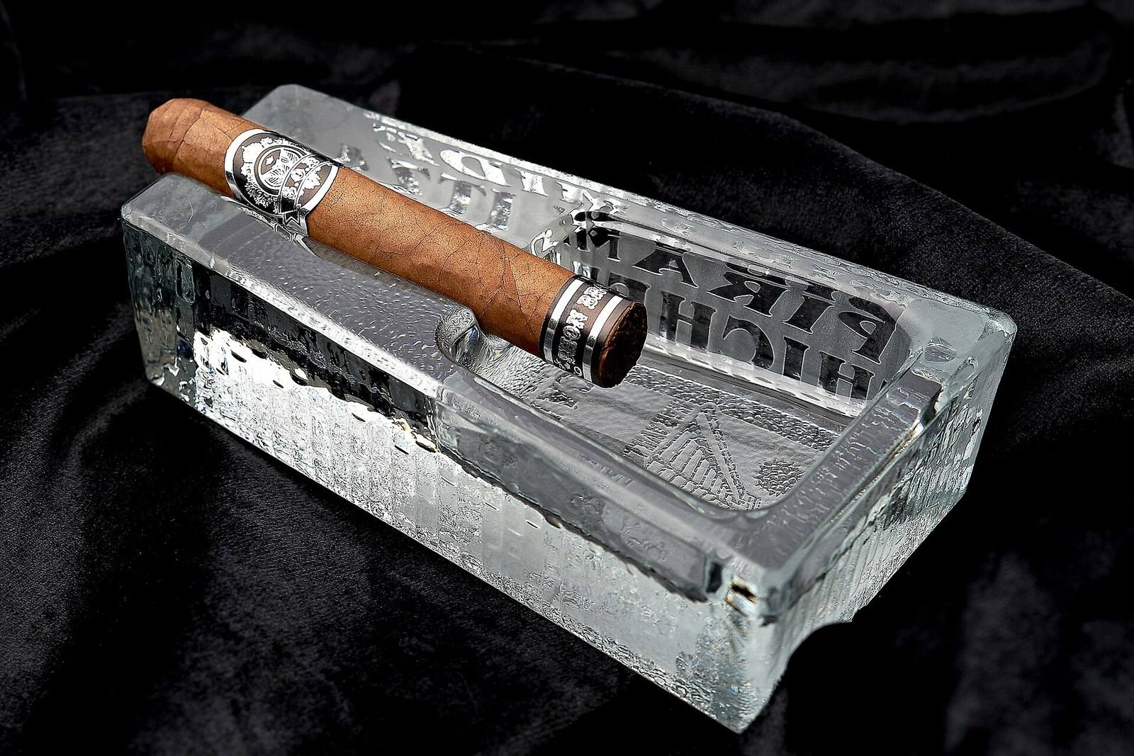 A lit cigar resting in a glass ashtray against a dark background