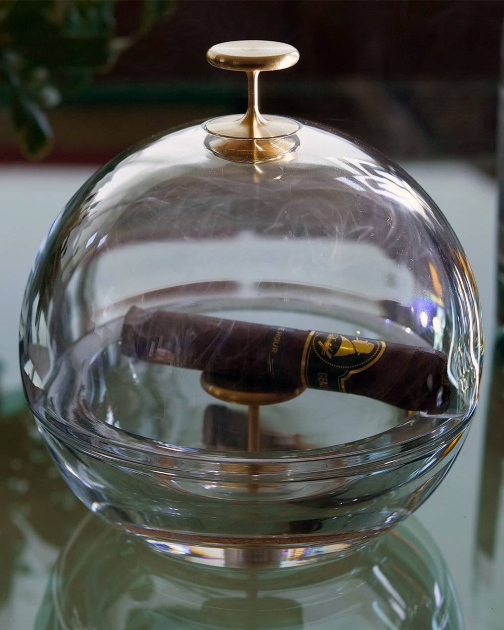 A cigar resting under the crystal dome of the Murmmr ashtray, seen close up