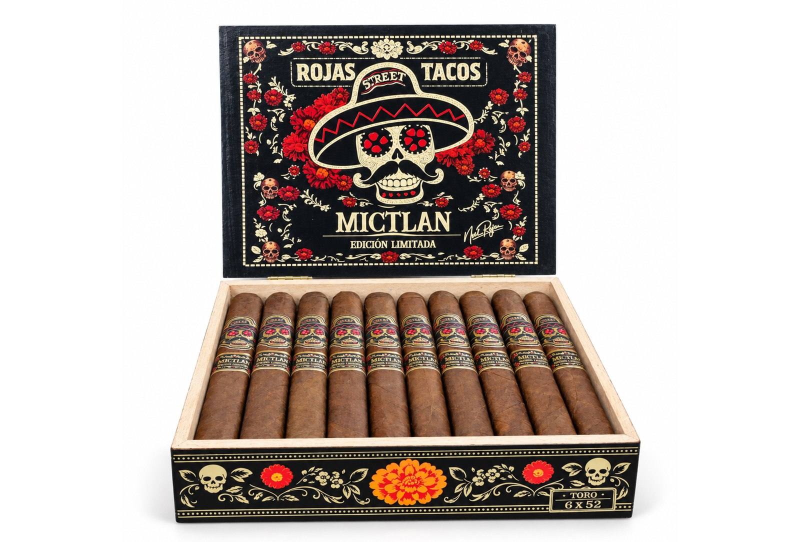 An open box of Rojas Street Tacos Mictlan cigars with skull bands, under a black lid decorated with marigolds and a skull in a sombrero