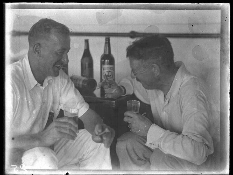 Two men laughing over beer and cigars aboard the SS Tanda