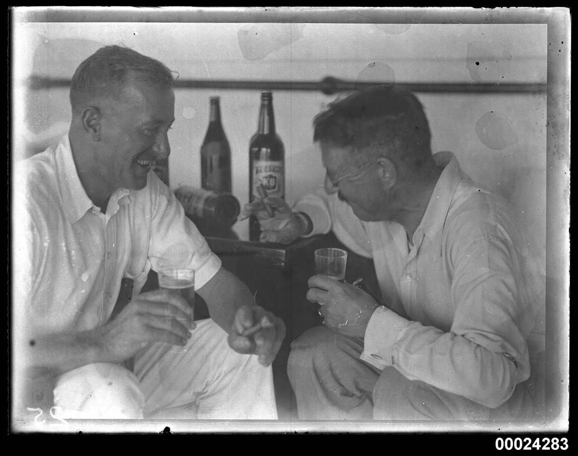Two men laughing over beer and cigars aboard the SS Tanda