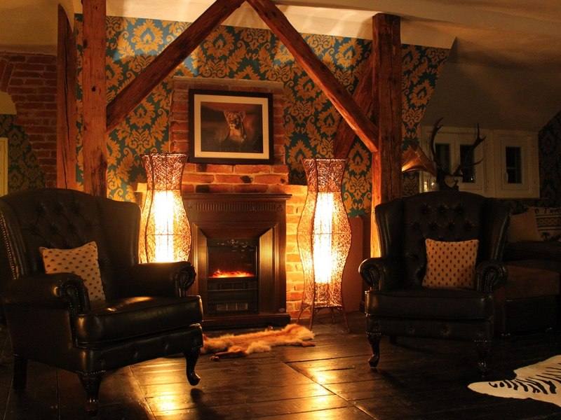 Warm cigar lounge with leather wingback chairs beside a lit fireplace
