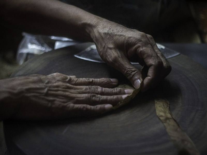 A torcedor's hands smoothing wrapper leaf on the rolling table