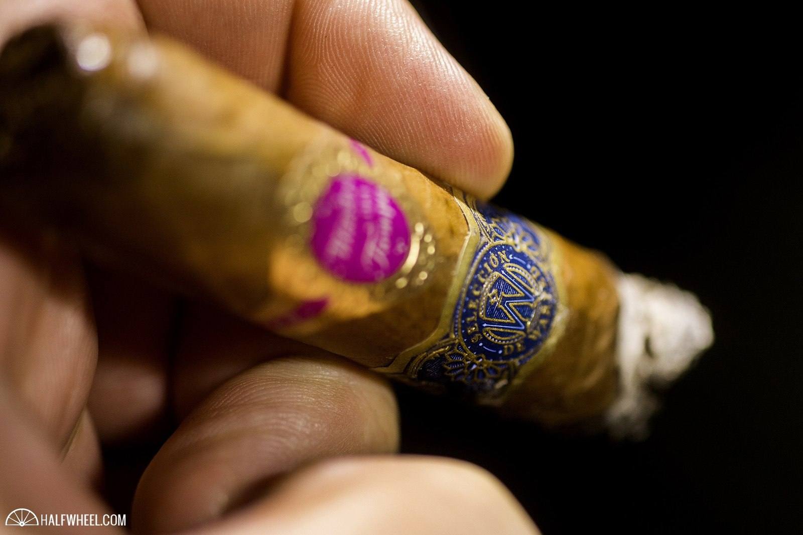 A Maestro del Tiempo 6102R cigar held in a hand, showing its blue and gold band, in halfwheel photography