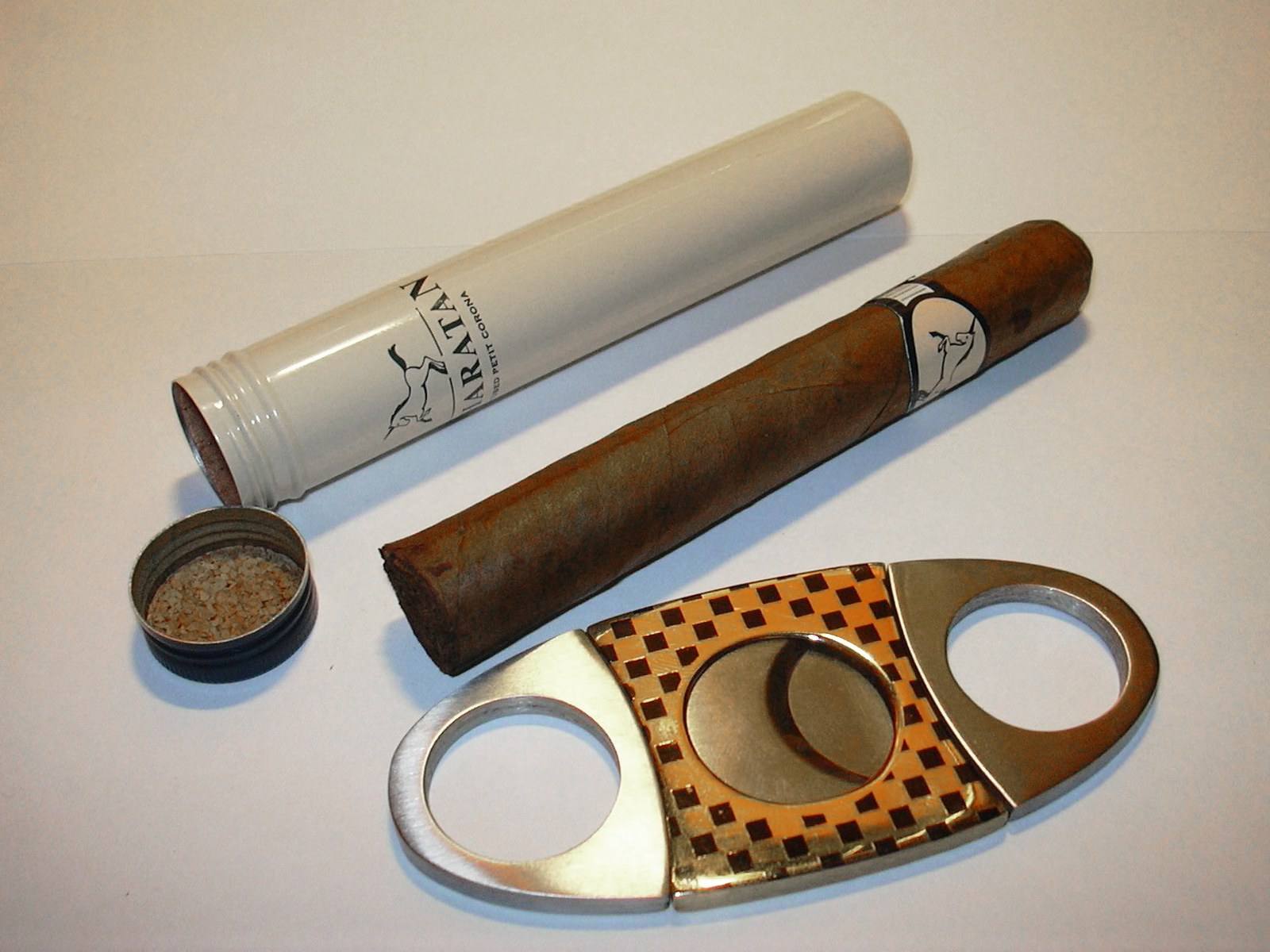 Double-blade guillotine cigar cutter beside a cigar and its tube